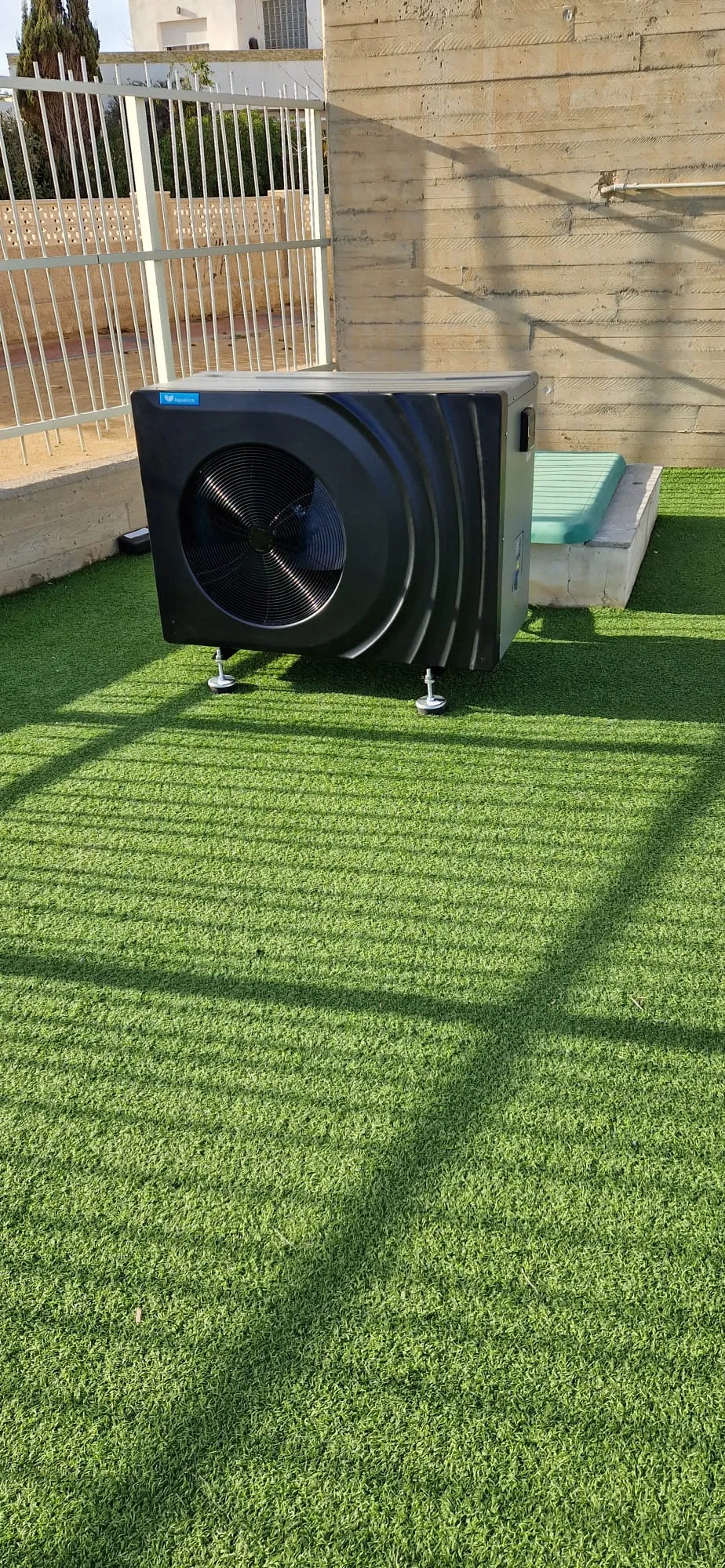 Bomba de calor negra para piscina instalada en una terraza con césped artificial