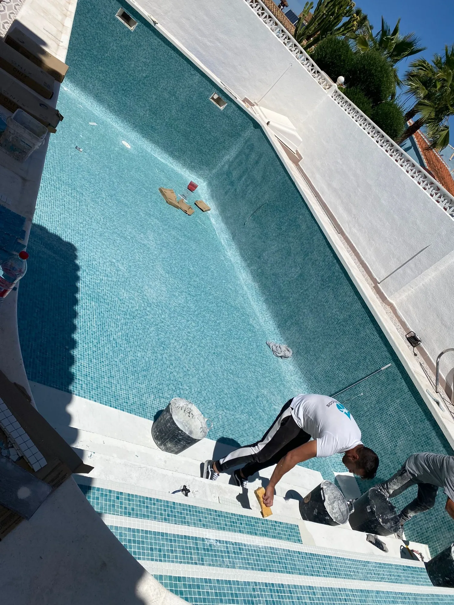 Operario colocando gresite verde agua en la escalera de una piscina vacía