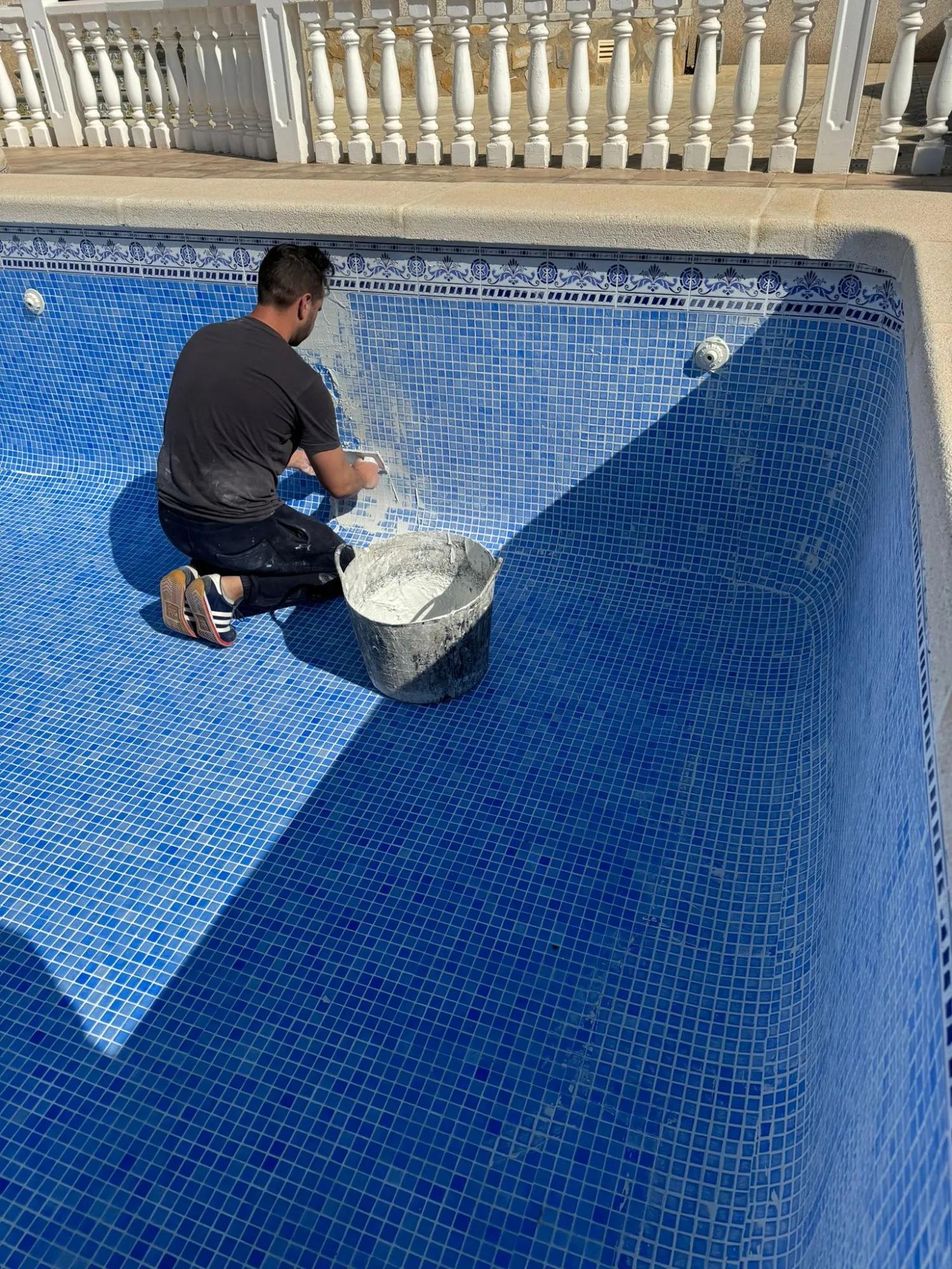 Operario de rodillas en un vaso de gresite azul aplicando la lechada